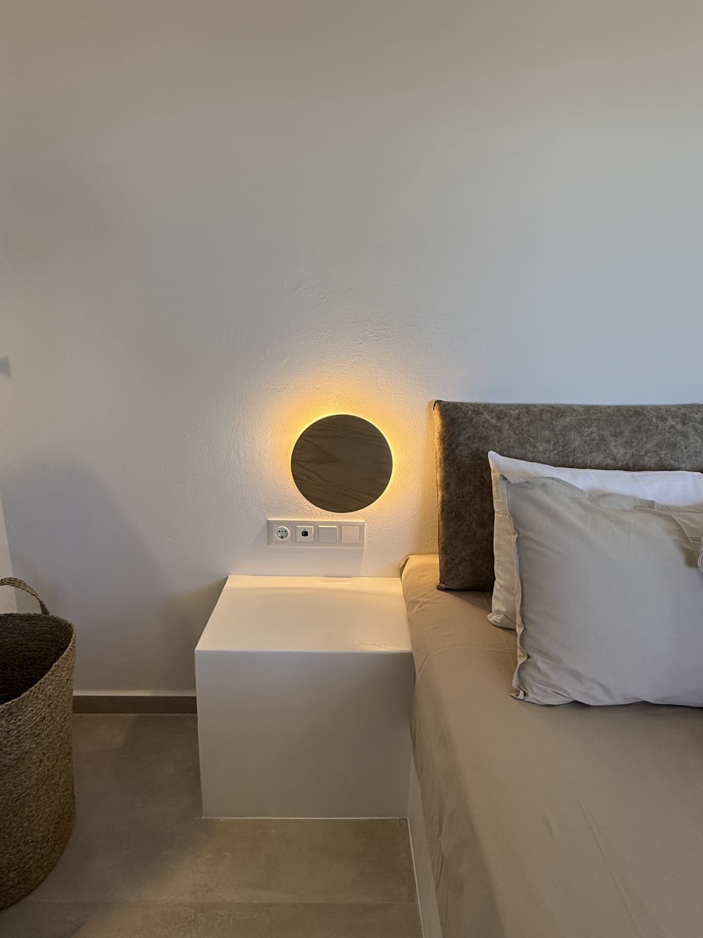 A bedside at DEON at night, a round wall light glowing against white plaster