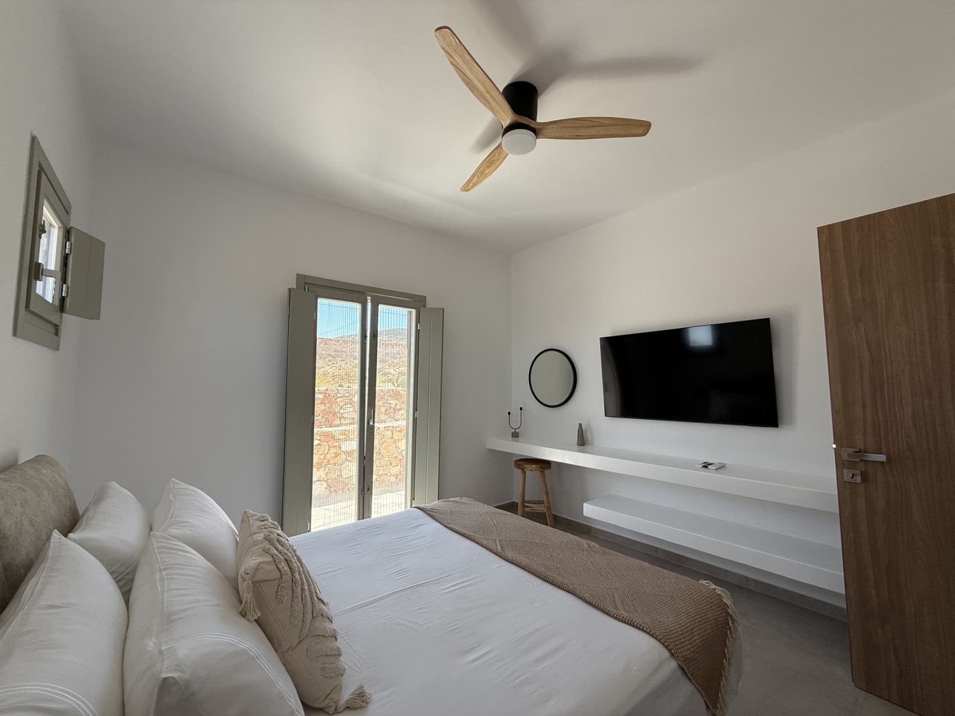 A bedroom at DEON, white linen and shuttered doors opening to the stone wall outside